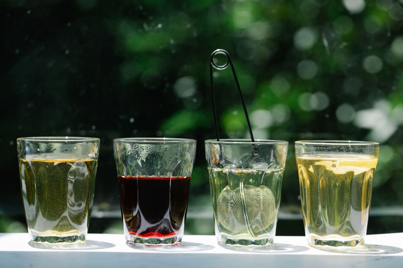 四個不同草本茶杯搭配茶濾器,呈現不同茶類對比,呼應寒熱體質選茶概念 | Four different herbal tea cups with strainers, showcasing tea type comparison relevant to cold-heat body constitution selection