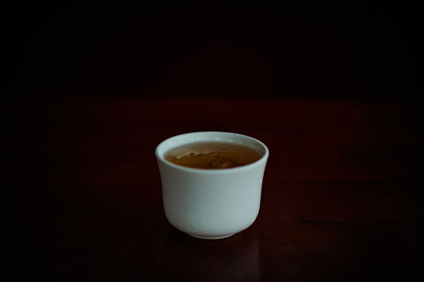 極簡風格的瓷杯盛滿黃亮茶湯,深色背景襯托出溫暖色澤 | A minimalist porcelain cup filled with yellow tea liquor against a dark background
