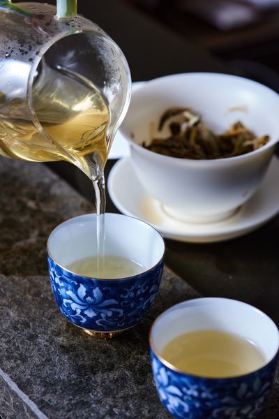 玻璃壺中茶水傾注藍色瓷杯,展現台灣高山茶沖泡的雅緻儀式 | Tea pouring from glass pot into blue porcelain cup showcasing elegant Taiwan oolong brewing ritual